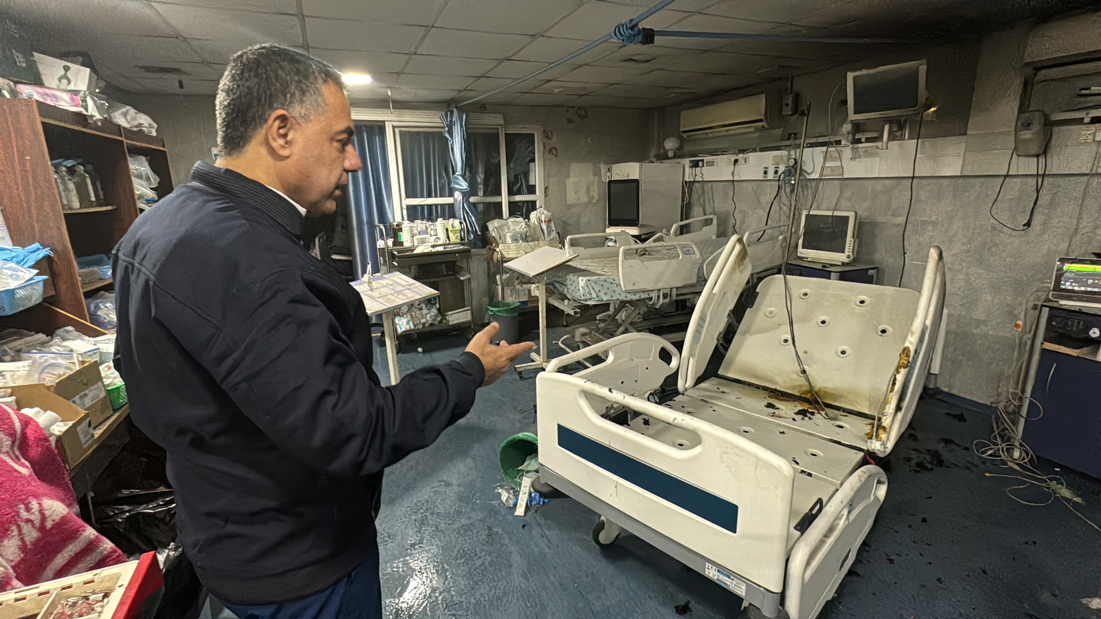 man stands over a damaged hospital bed in kamal adwan hospital 
