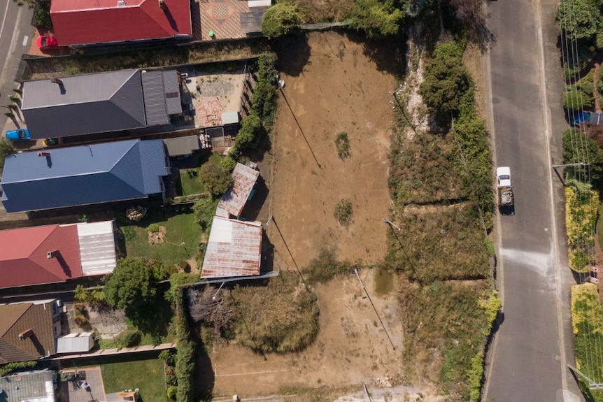 An aerial picture of an old tennis court with houses and a road nearby