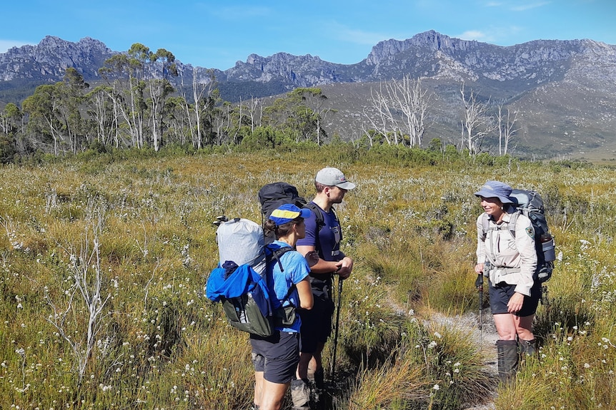 A ranger talking to two bushwalkers in a remote Tasmanian location, mountains in the background.