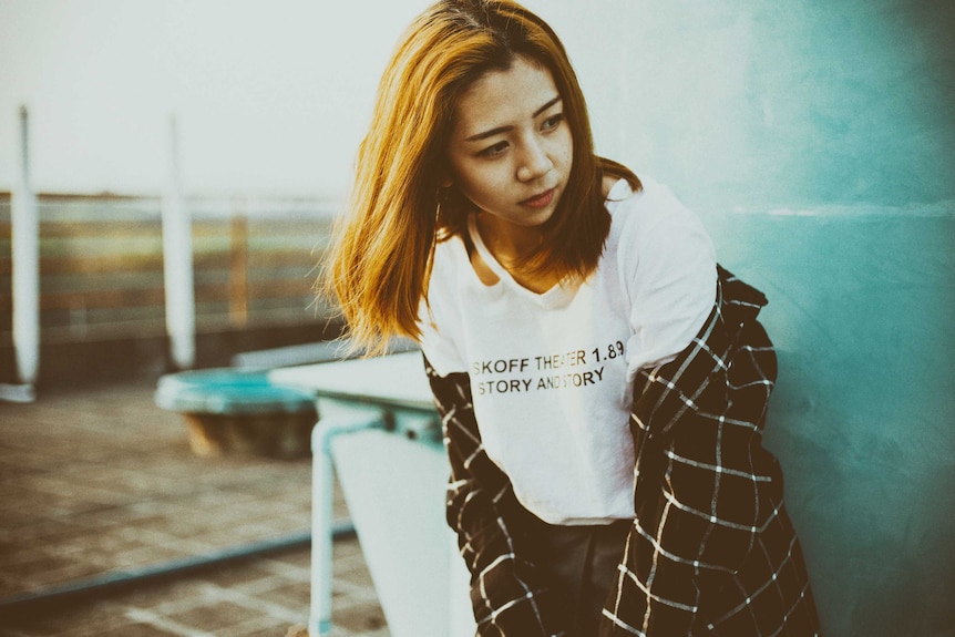 Woman stands against concrete wall wearing check shirt