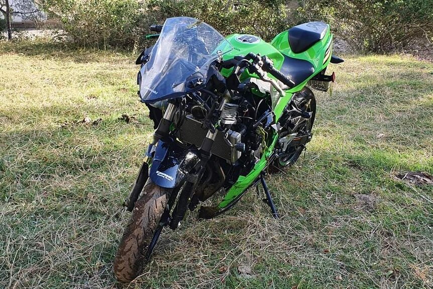 a damaged green motorbike sitting on the grass after a crash