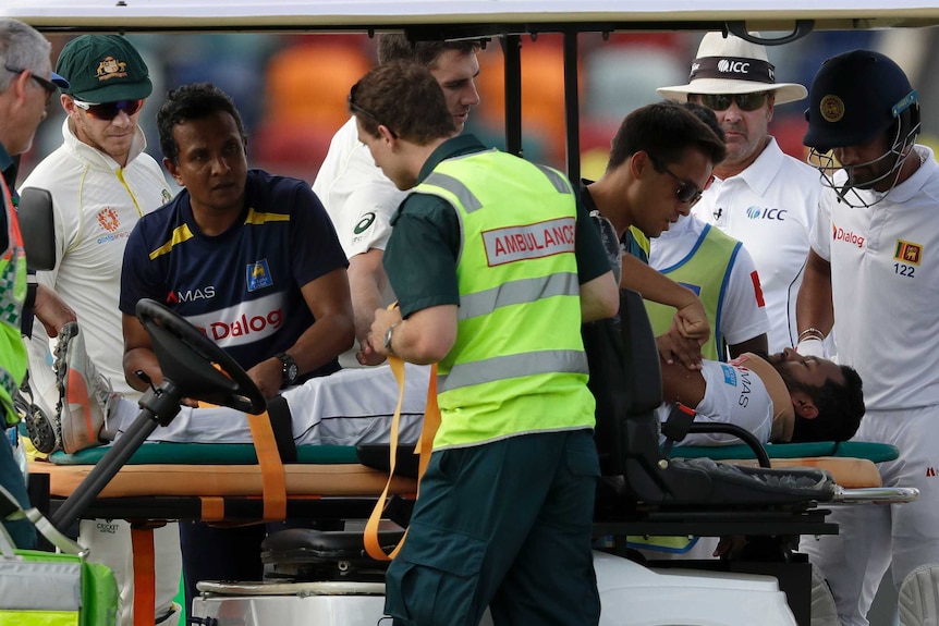 Australia cricketers Tim Paine (second from left) and Pat Cummins (centre) check on Dimuth Karunaratne while he's on a medicab.