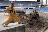 View from inside the Rio Olympic Stadium of workers and construction underway, with seating in place in the background.