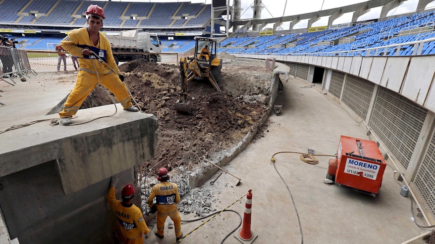 View from inside the Rio Olympic Stadium of workers and construction underway, with seating in place in the background.