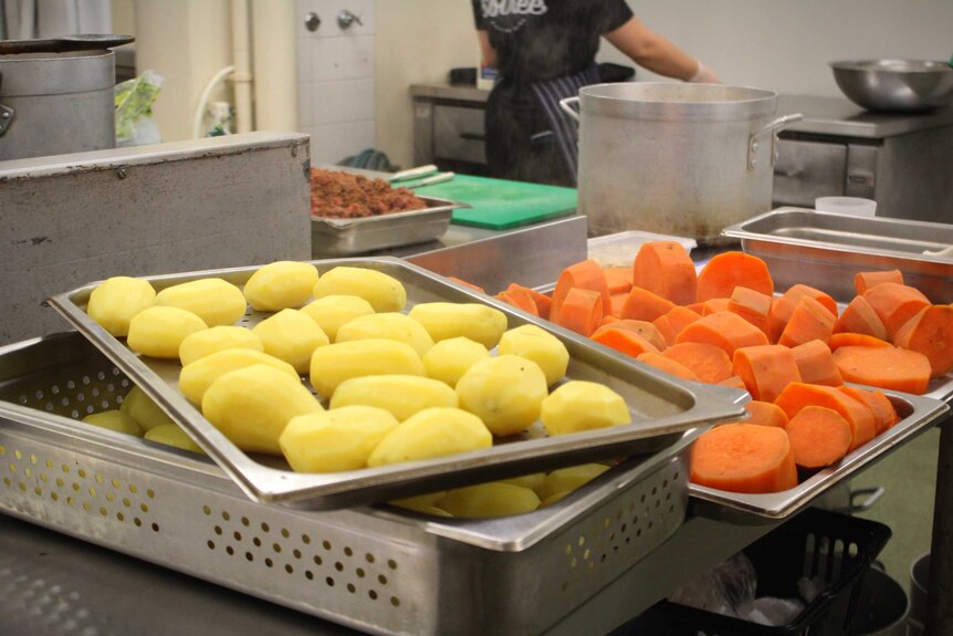 Carrots and potato sit on trays inside a commercial kitchen