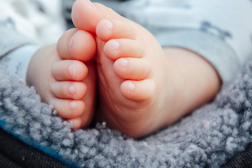 The clasped feet of a ten-month-old baby boy on a blue rug.