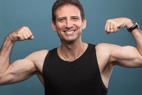 Universal Medicine founder Serge Benhayon smiles at camera in singlet, flexing his muscles.