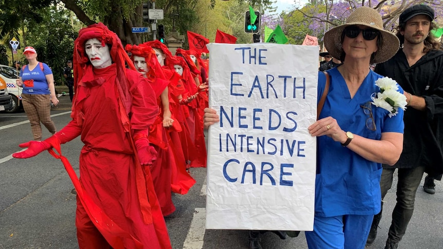 Protesters dressed in red with red face paint alongside a woman holding a sign saying Earth needs intensive care