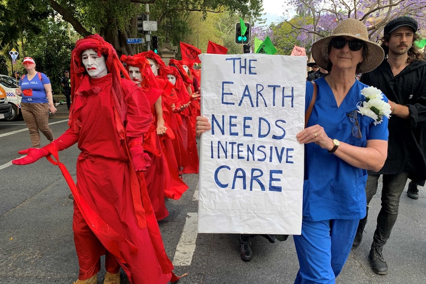 Protesters dressed in red with red face paint alongside a woman holding a sign saying Earth needs intensive care