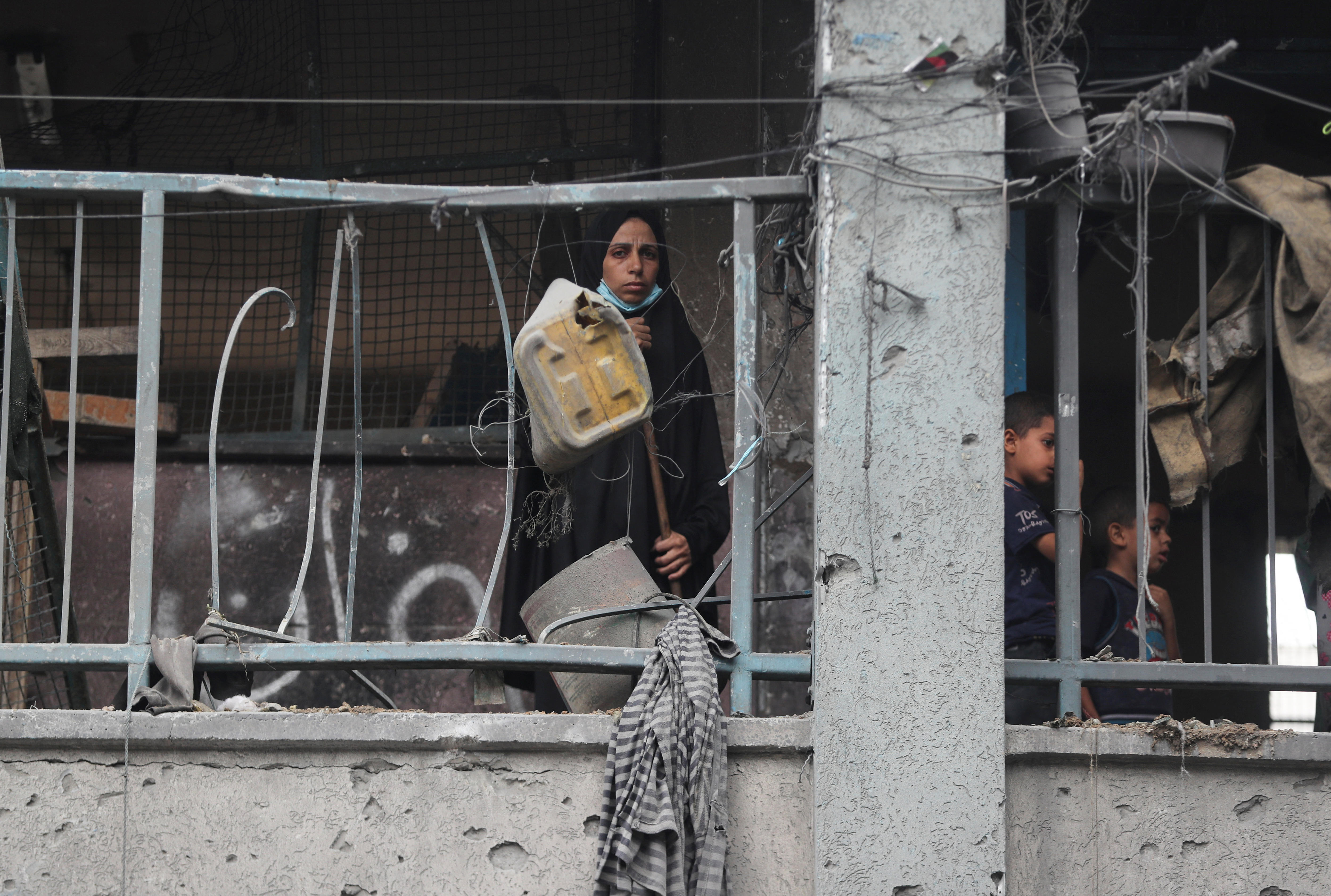 A Palestinian woman looking at the camera from a partially destroyed balcony.