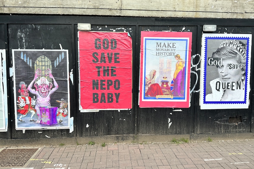 Posters are tacked onto a wall by a footpath. One reads 'god save the nepo baby', another 'make monarchy history'