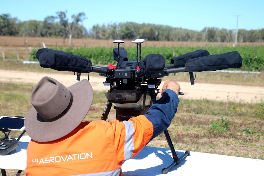 A man with a big hat is working on a drone with six propellers on a table.