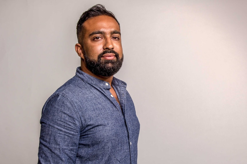 Osman Faruqi wears a dark denim shirt. He is against a grey background and looks at camera. He has dark, short hair and a beard.