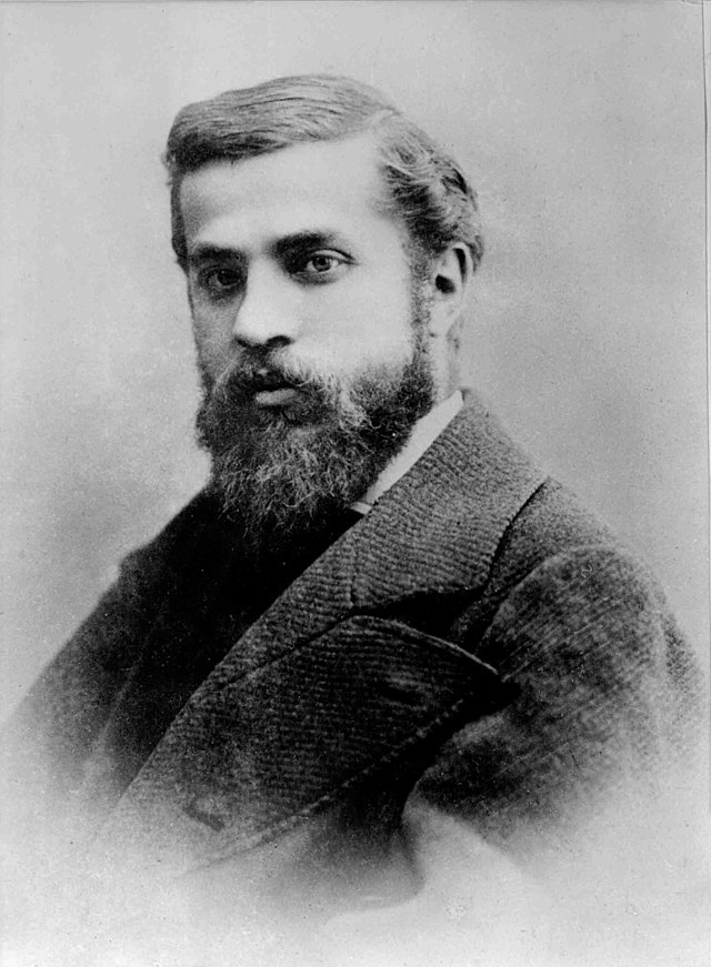 A very old looking black and white portrait photo of a young bearded man wearing a jacket