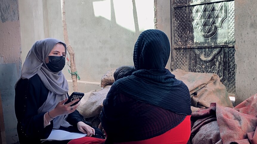 A female reporter in a hijab and facemask interviews a survivor of floods in Baghlan province, Afghanistan.