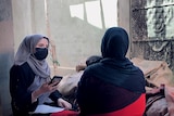 A female reporter in a hijab and facemask interviews a survivor of floods in Baghlan province, Afghanistan.