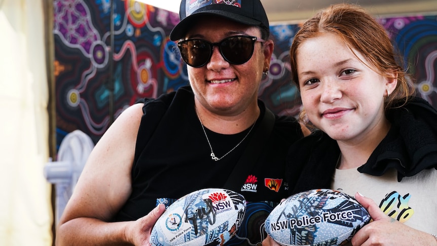 A woman and a young girl holding signed rugby league balls.