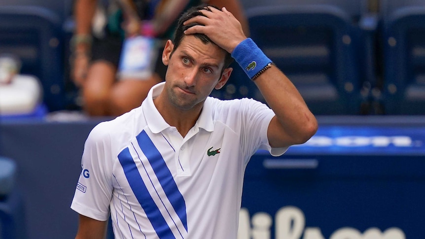 A stunned-looking tennis player stands with his hand on his head after an on-court incident.