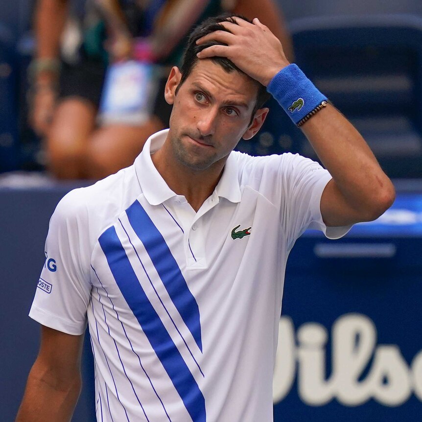A stunned-looking tennis player stands with his hand on his head after an on-court incident.