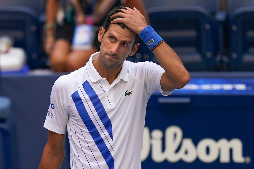 A stunned-looking tennis player stands with his hand on his head after an on-court incident.