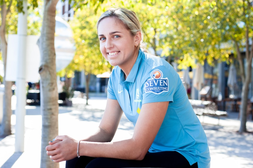 Young woman sits on a bench, she is smiling.