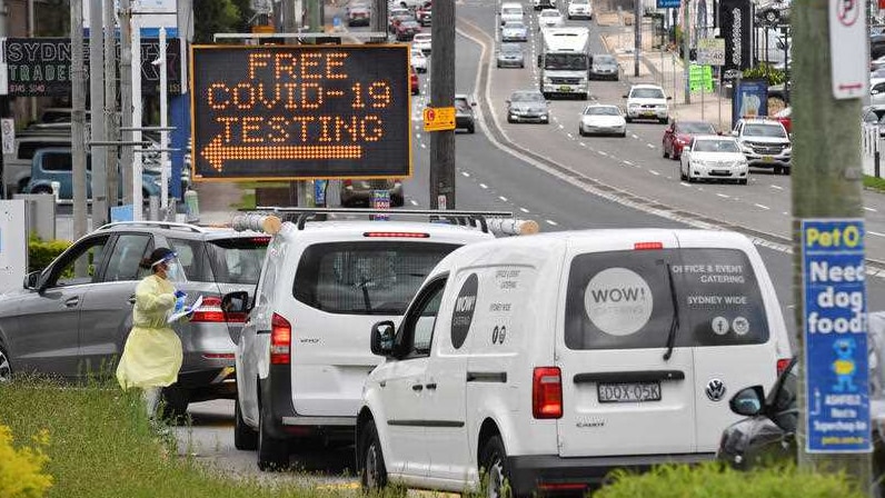 A line of cars under a COVID testing sign on a big road.