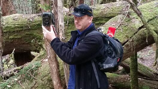 Warren Darragh with a motion sensing camera in the Tasmanian bush.