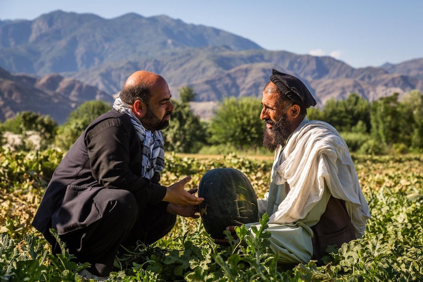 Afghan journalist Bilal Sarwary crouches down as he speaks to an Afghan farmer.