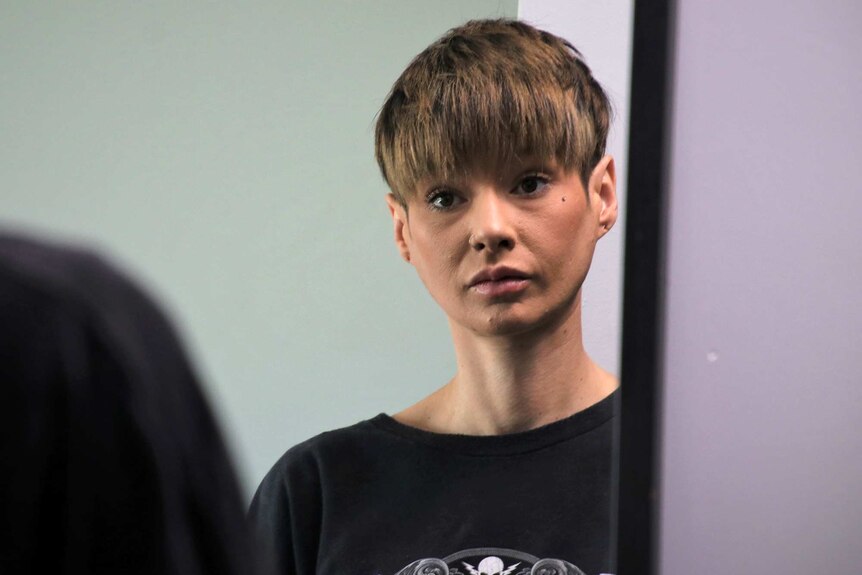 A head and shoulders shot of a woman with short hair wearing a black shirt looking in a mirror.