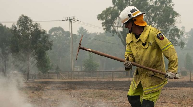 A firefighter stands on smouldering ground  in Wingello.