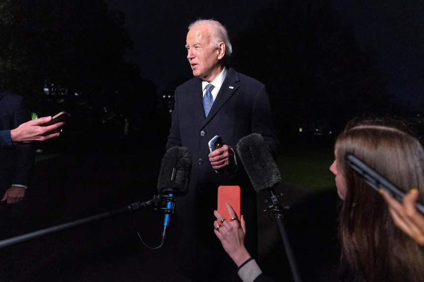 President Joe Biden speaks to the media on the South Lawn of the White House at night.