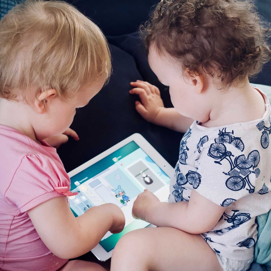 two toddlers play with a ipad