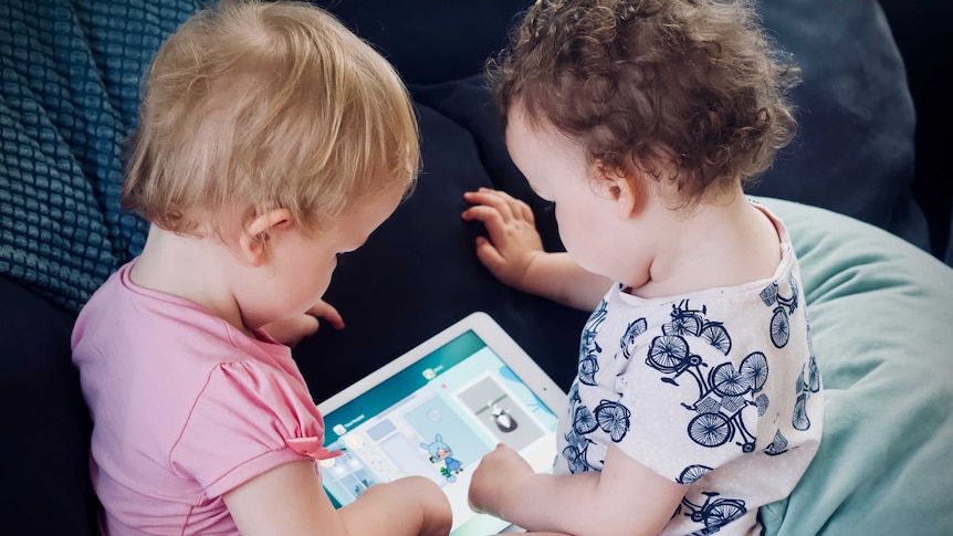 two toddlers play with a ipad