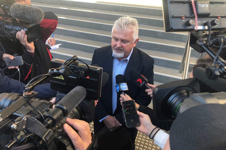 A man speaks to a large group of media.