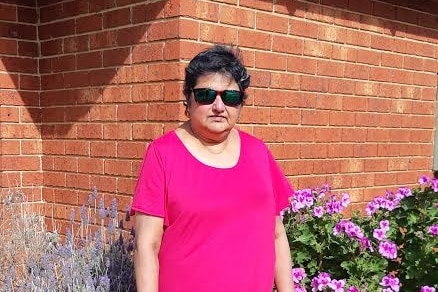 A woman wearing a pink top and sunglasses in front of a brick wall. 
