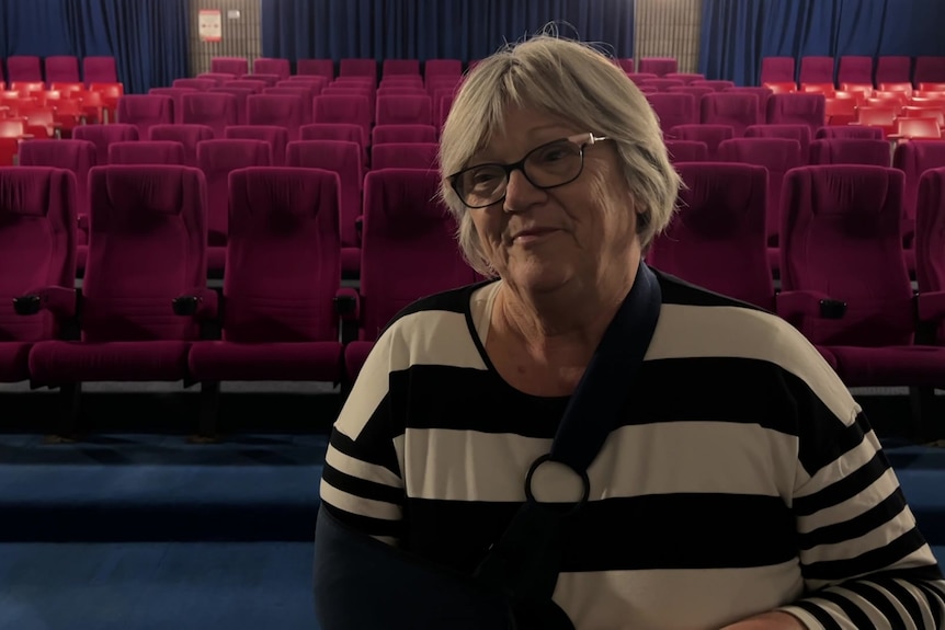 a woman with glasses in a strip top and her hand in a sling in a cinema
