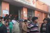 Dozens of people wait outside a hospital, while a person on a stretcher is taken inside