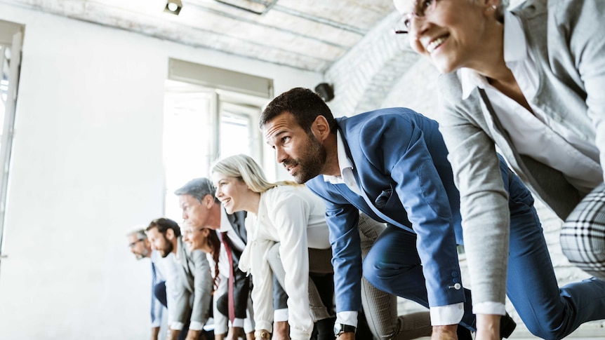 A group of men and women in business clothes crouched ready to run on a starting line