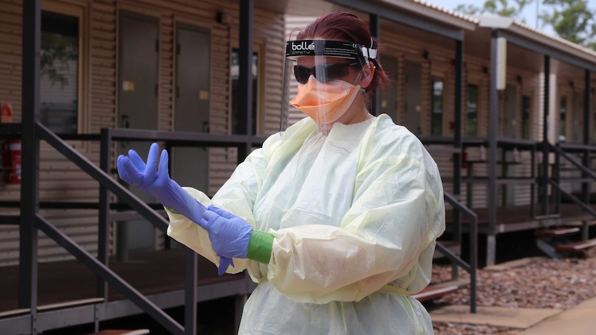 A health worker in full PPE puts on some gloves outside near some dongas in the Howard Springs quarantine facility.