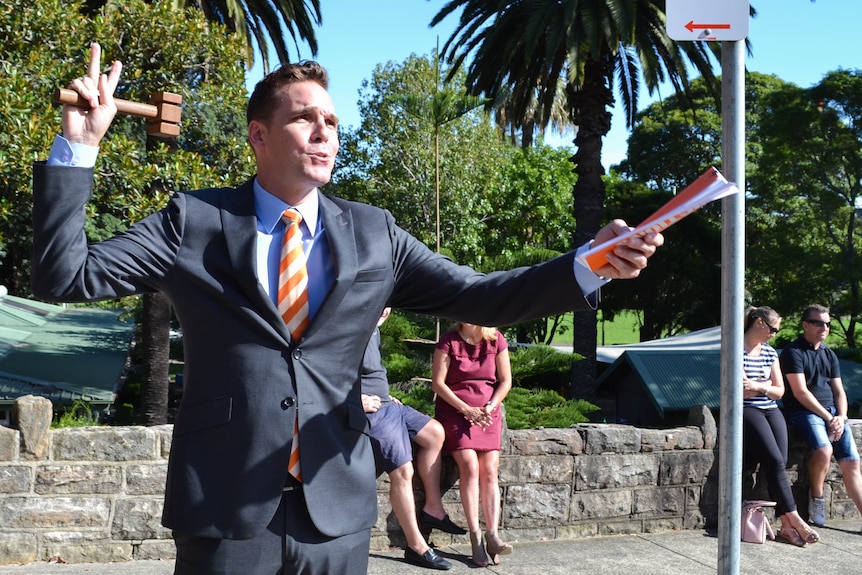 Toby Llewellyn holds a gavel up in his hand as he talks.