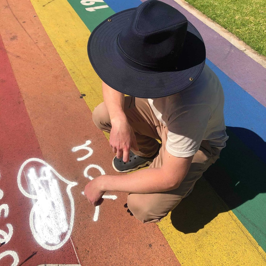 A man sitting near white spray paint messages on a rainbow path