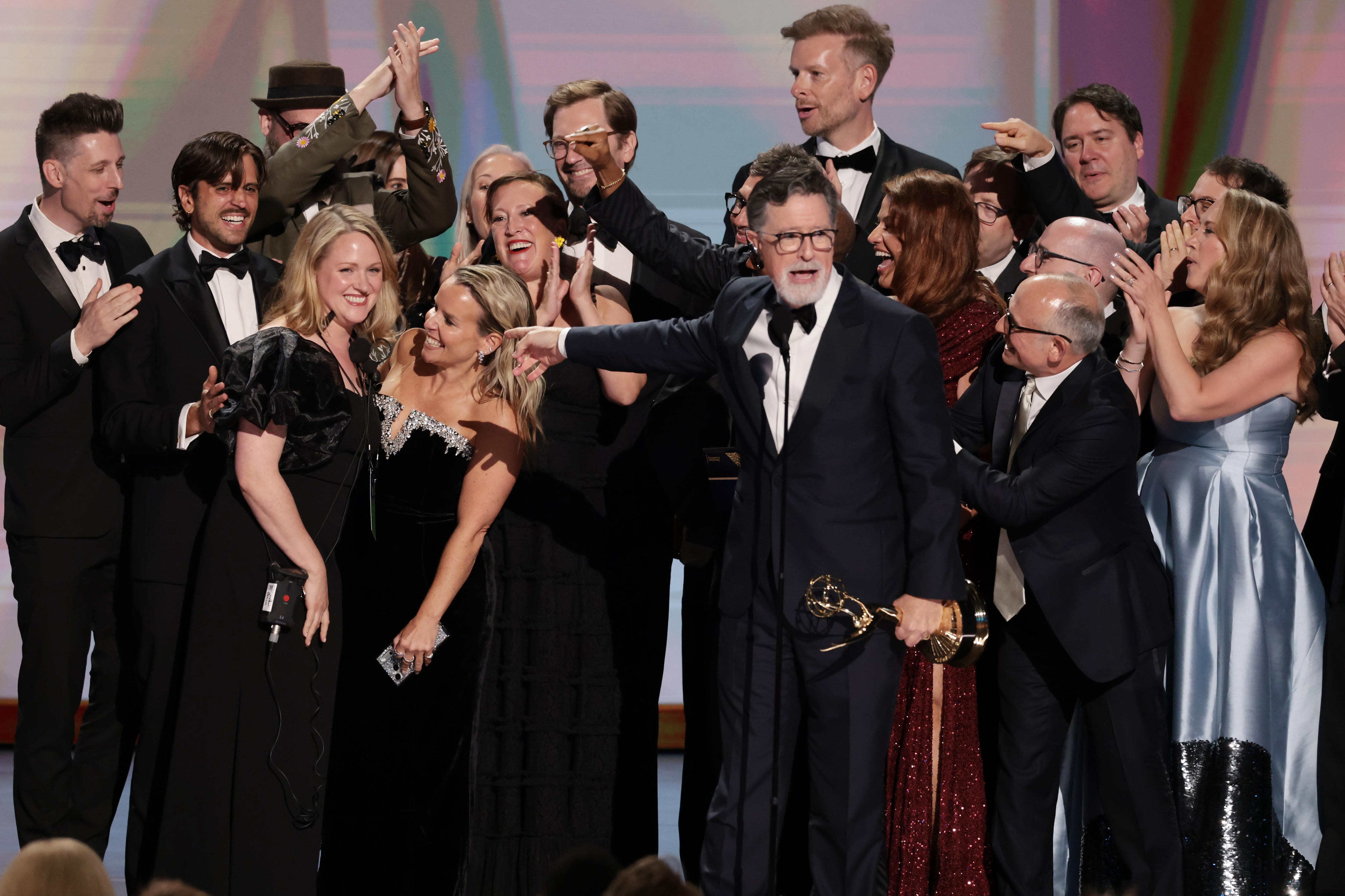 Stephen Colbert with a big group of people behind him holding an Emmy