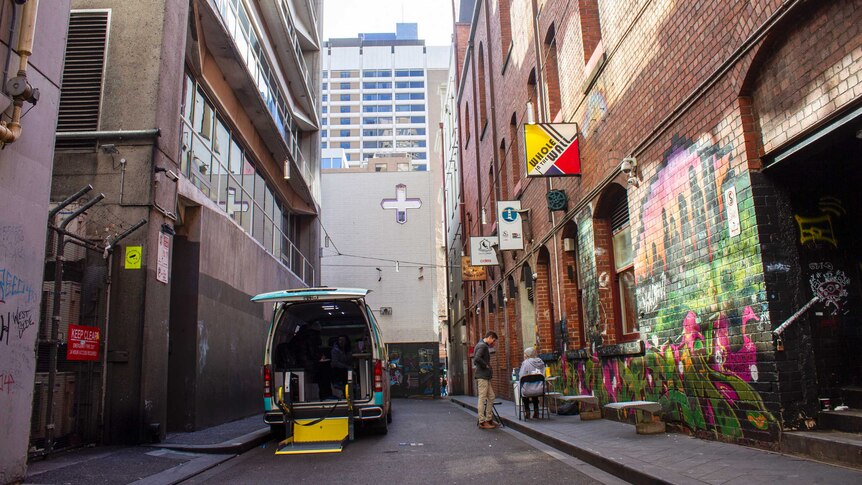 A van with its backdoor open parked in a narrow alleyway.