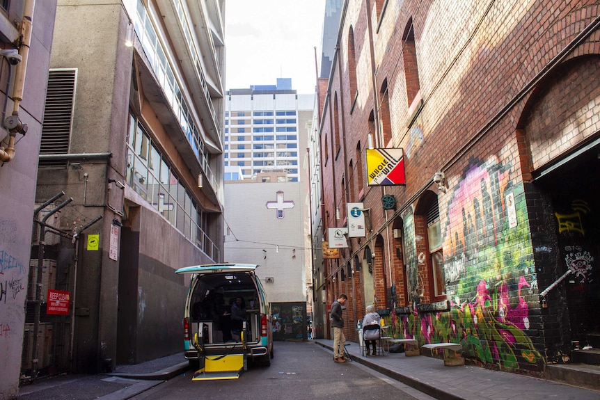 A van with its backdoor open parked in a narrow alleyway.