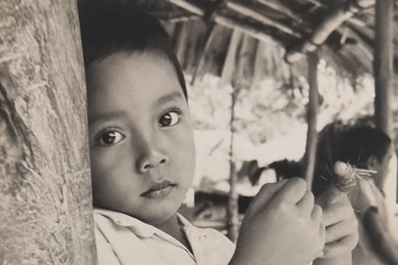 Black and white photo of young child leaning against a wooden beam with serious expression.