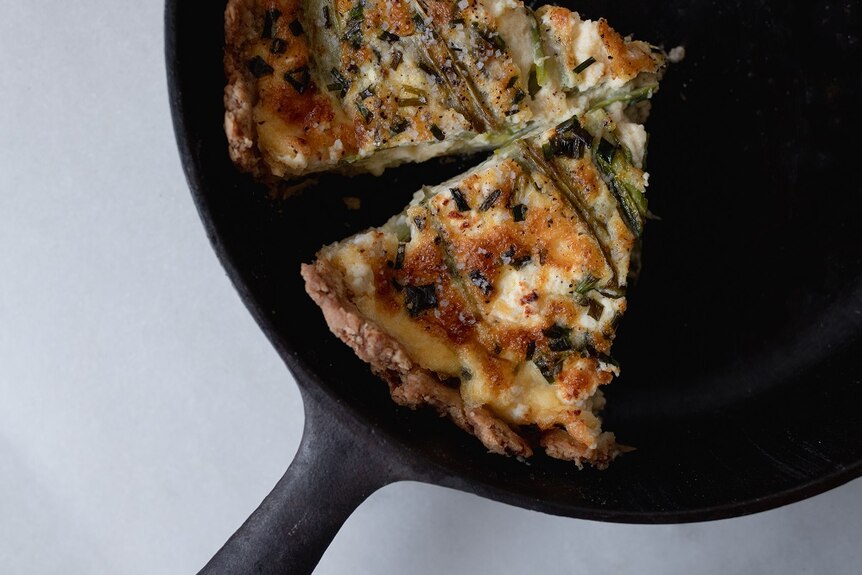 Two slices of asparagus and goat cheese quiche topped with salt in a cast iron skillet, a decadent but easy lunch or dinner.