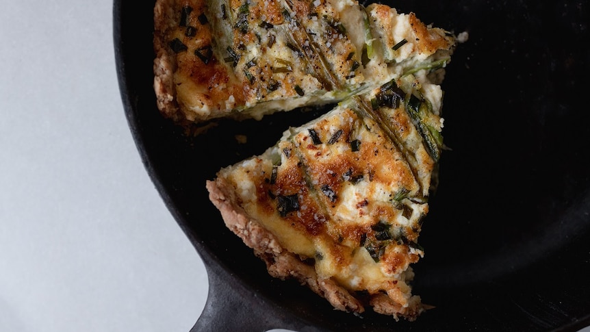 Two slices of asparagus and goat cheese quiche topped with salt in a cast iron skillet, a decadent but easy lunch or dinner.