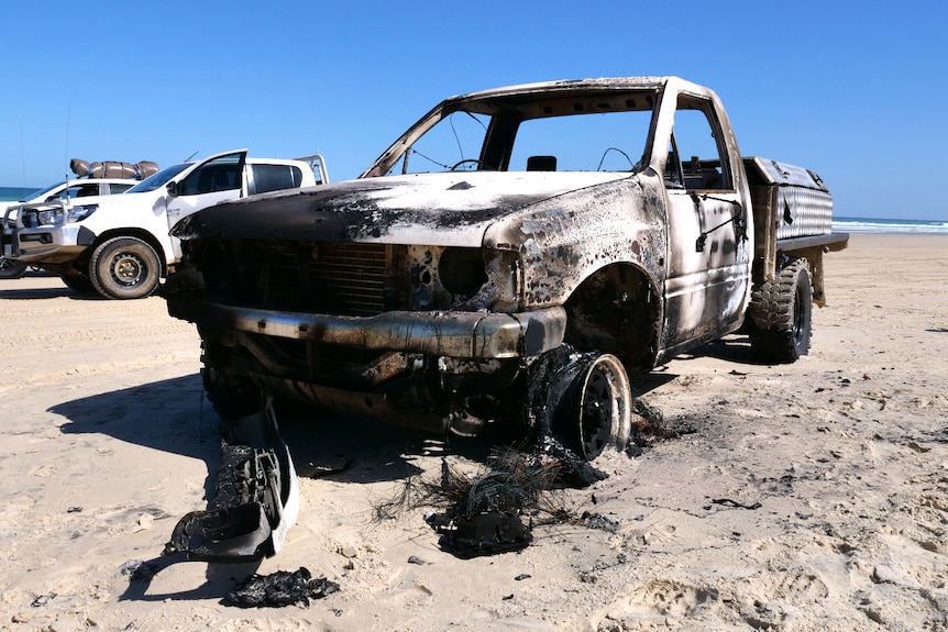 The burnt out wreck of a car sits on a sandy beach