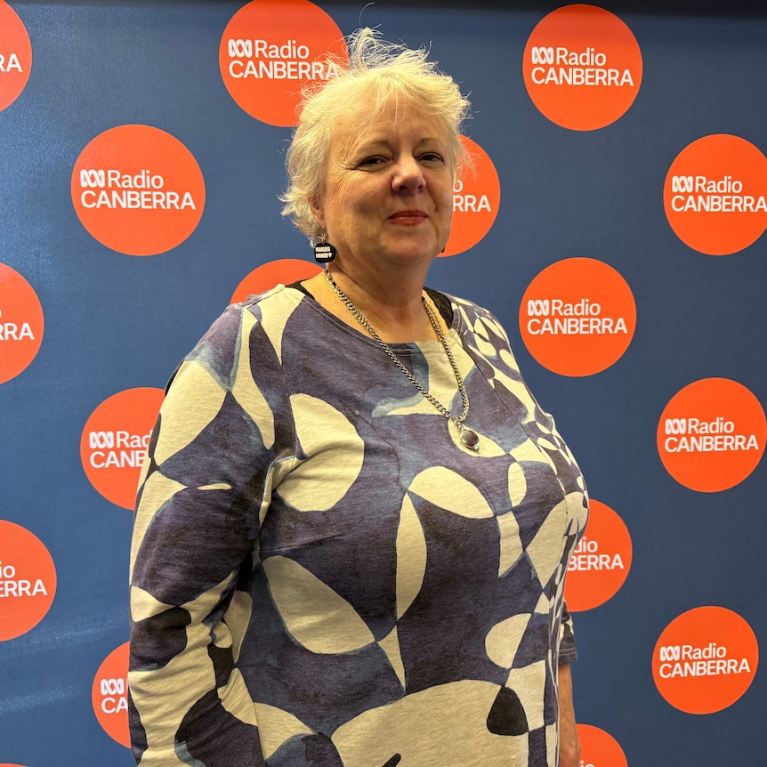 Glenda Stevens, CEO of Fearless Women wears blue and white circular patterned top standing against ABC radio backdrop
