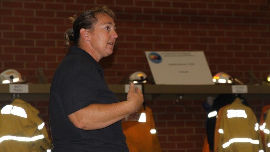 A woman stands to speak to a crowd of prospective firefighter volunteers